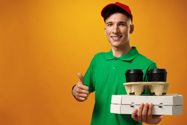 Happy young delivery man holding pizza box against yellow surface