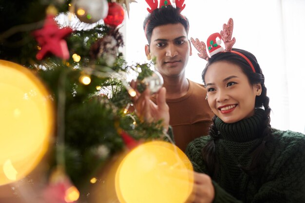 Happy young diverse couple decorating Christmas tree for celebration