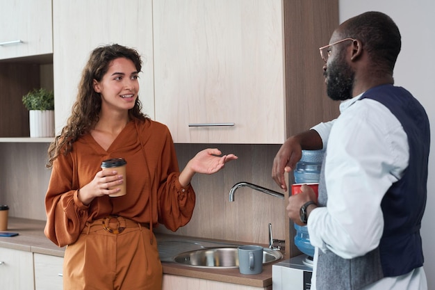 happy young elegant businesswoman with cup of coffee talking to colleague