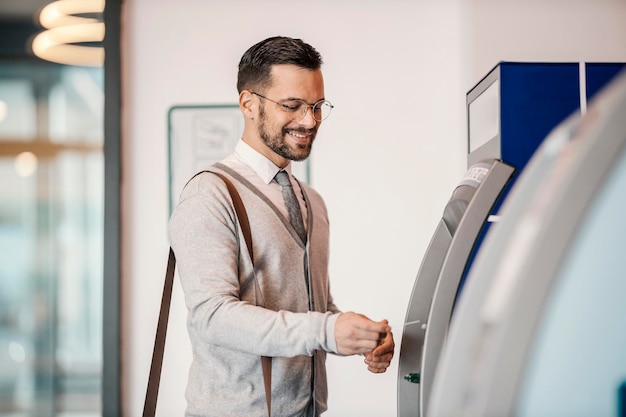 a happy young elegant man is using atm in a mall
