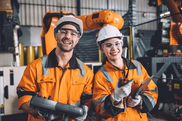 Photo happy young engineer working together service team with robot welding in automation factory man and woman smiling worker in safety suit staff worker in automated technology manufacturing industry