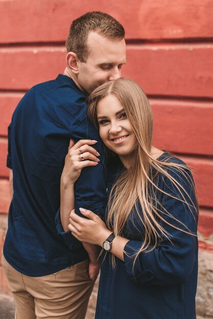 Happy young family on the background of a red wall. Young woman laid her head on her man's shoulder