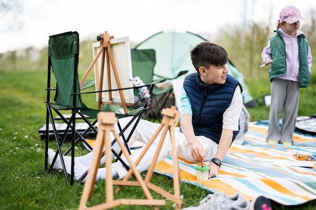 Felice giovane fratello e sorella di famiglia che si divertono e si divertono all'aperto sulla coperta da picnic che dipinge su tela al relax del parco primaverile del giardino