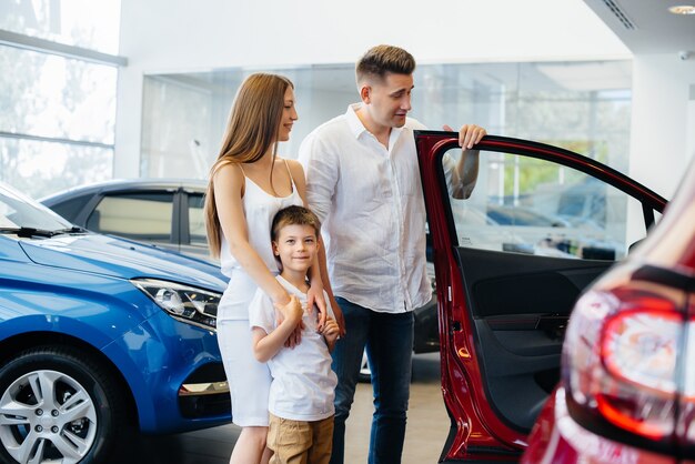 Счастливая молодая семья выбирает и покупает новую машину в автосалоне.