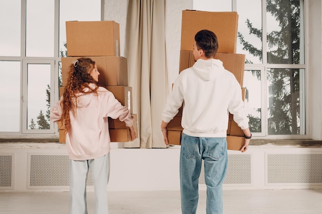 Photo happy young family couple man and woman moving with cardboard boxes to new estate home apartment rear back view