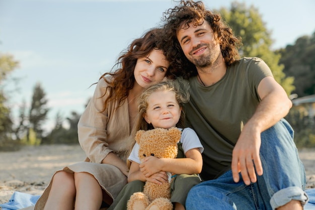 Happy young family enjoys their vacation on a sunny beach with cute teddy bear