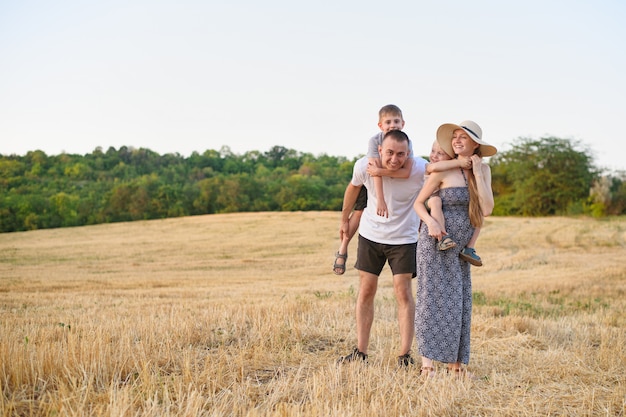 Happy young family. A father, a pregnant mother, and two little sons on their backs. Beveled wheat field