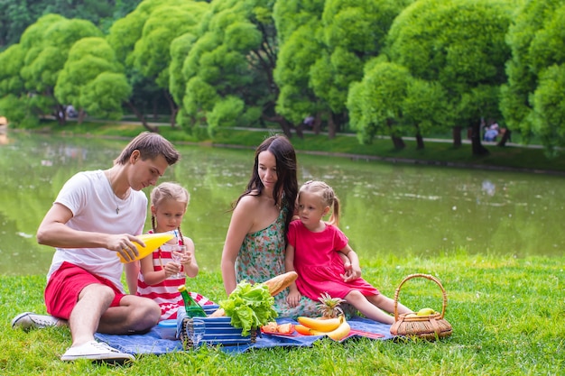 Happy young family of four picnicking near the lake