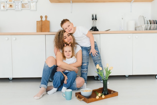 Happy young family, mom with little children sit on the floor in the kitchen