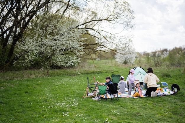 행복한 젊은 가족 어머니와 4명의 자녀가 정원 스프링 공원 휴식 공간에서 피크닉 담요 그림을 그리며 야외 활동을 즐기고 있습니다.