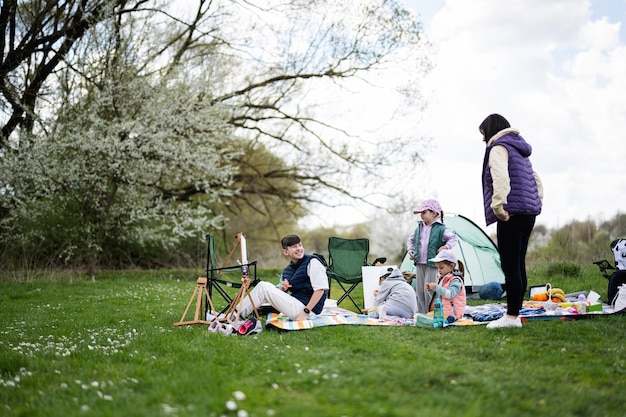 Happy young family mother and four children having fun and enjoying outdoor on picnic blanket painting at garden spring park relaxation