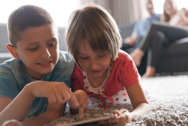 写真 幸せな若い家族が家で一緒に遊んでいます。床でタブレットを使用している子供たち