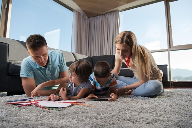 Foto felice giovane famiglia che gioca insieme a casa sul pavimento utilizzando un tablet e un set da disegno per bambini