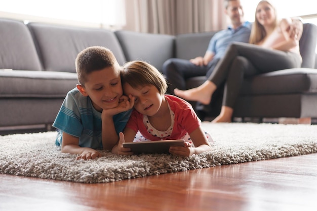 幸せな若い家族が家で一緒に遊んでいます。床でタブレットを使用している子供たち
