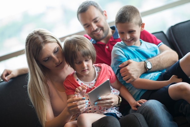 Счастливая молодая семья играет вместе с планшетом дома, сидя на диване.