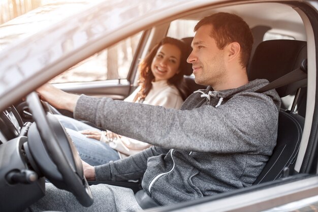 幸せな若い家族が森の中の車に乗る。男が車を運転していて、妻が近くに座っています。車のコンセプトで旅行