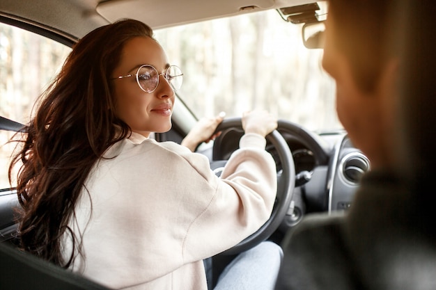 幸せな若い家族が森の中の車に乗る。女性が車を運転し、男性が近くに座っています。車のコンセプトで旅行