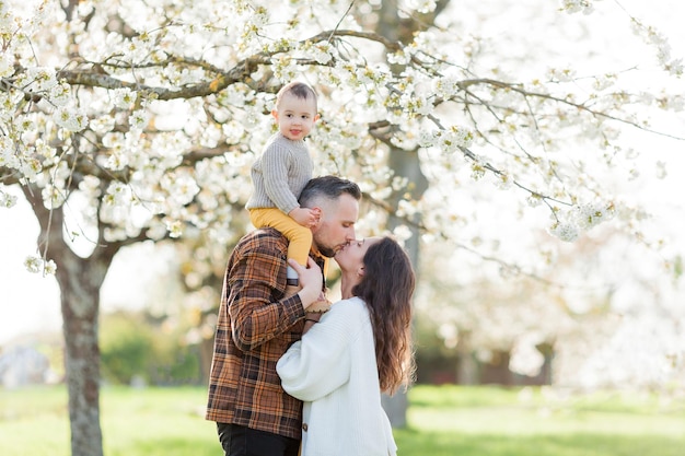 写真 春の花開く公園で過ごす幸せな若い家族 ママ パパと小さな息子が外で遊んでいます