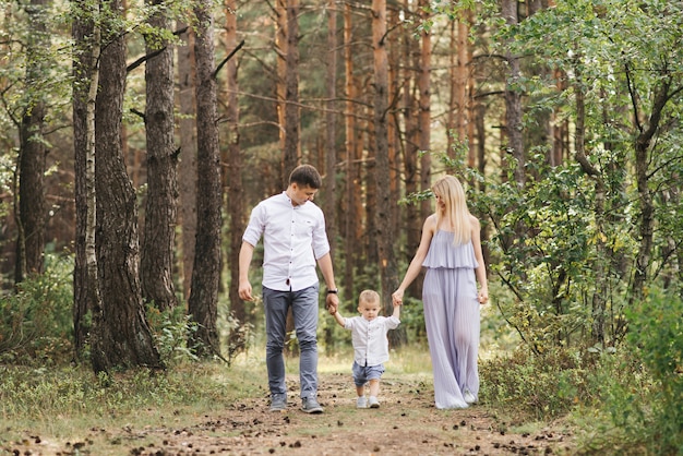 La giovane famiglia felice trascorre insieme il tempo in natura. i genitori vanno e tengono le mani del bambino