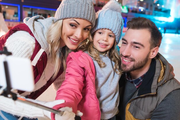 Felice giovane famiglia prendendo selfie con lo smartphone sulla pista di pattinaggio