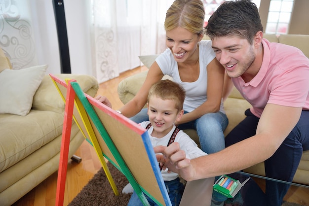 счастливая молодая семья преподает уроки и готовит сына к школе, рисуя дома на доске