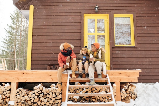 Photo happy young family of three sitting on wooden porch by their countryhouse