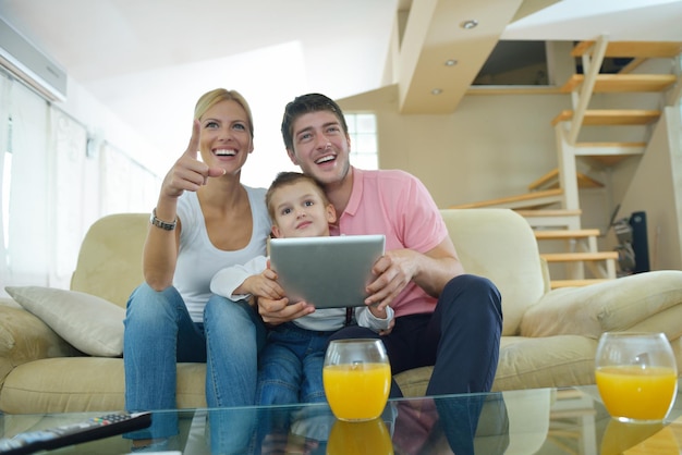 счастливая молодая семья, использующая планшетный компьютер в современном доме для игр и обучения