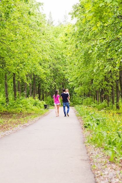 緑の自然の中で外の道を歩いて幸せな若い家族。