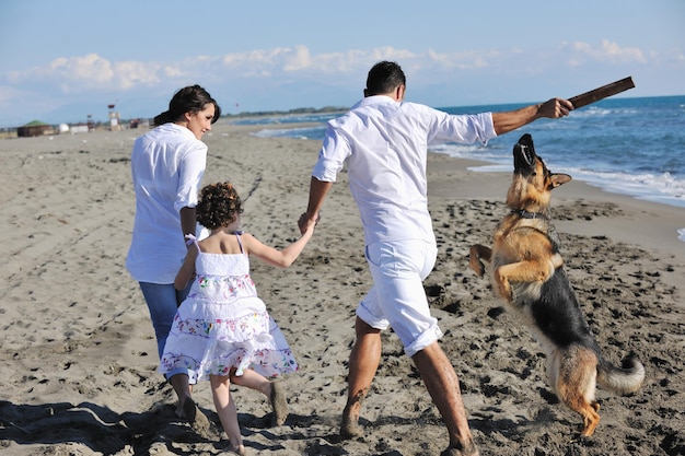 happy young family in white clothing have fun and play with beautiful dog at vacations on beautiful beach