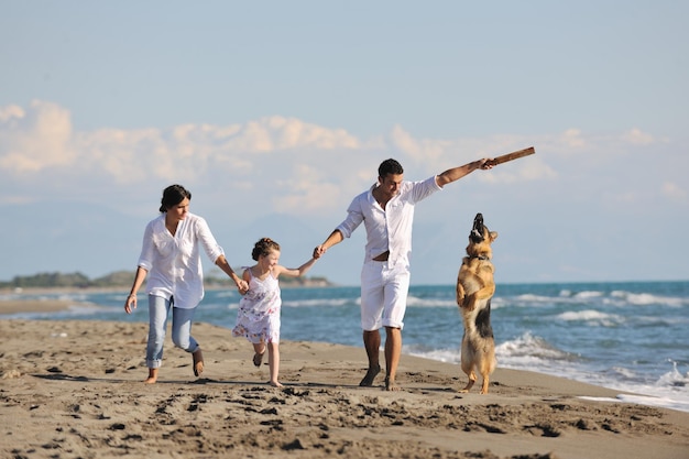 La giovane famiglia felice in abiti bianchi si diverte e gioca con un bel cane in vacanza sulla bellissima spiaggia