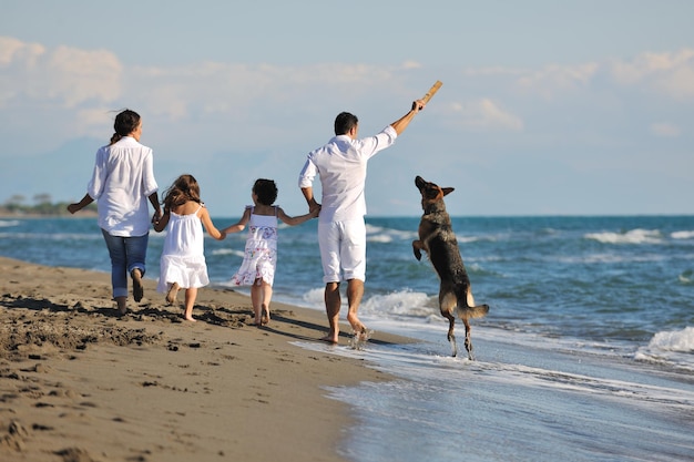 하얀 옷을 입은 행복한 젊은 가족은 아름다운 해변에서 휴가를 보낼 때 아름다운 개와 즐겁게 놀고 있습니다