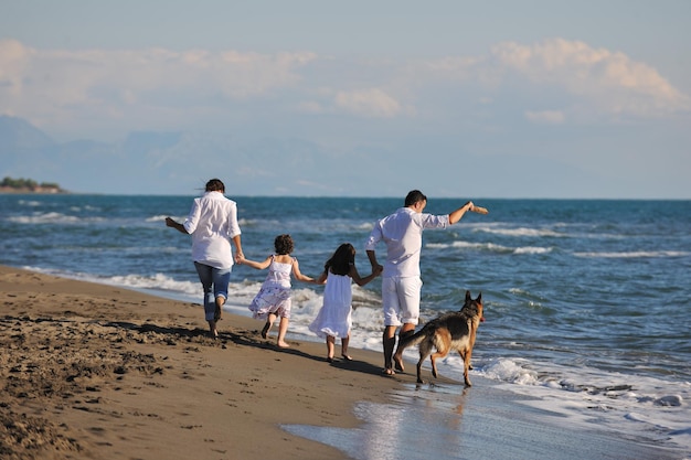 하얀 옷을 입은 행복한 젊은 가족은 아름다운 해변에서 휴가를 보낼 때 아름다운 개와 즐겁게 놀고 있습니다