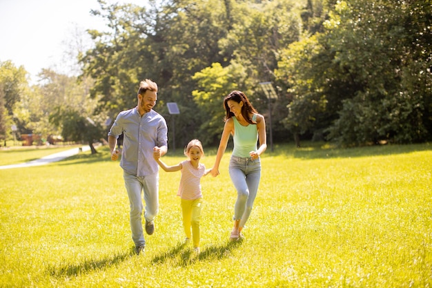 Счастливая молодая семья с милой маленькой дочерью, развлекающейся в парке в солнечный день
