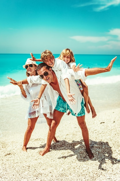 Happy young family with little kids having fun at the beach. Mom and dad piggyback their sons.