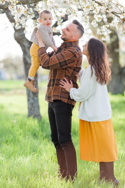 Happy young family with little son walks in blooming garden Mom and dad with 1 year old baby Spring