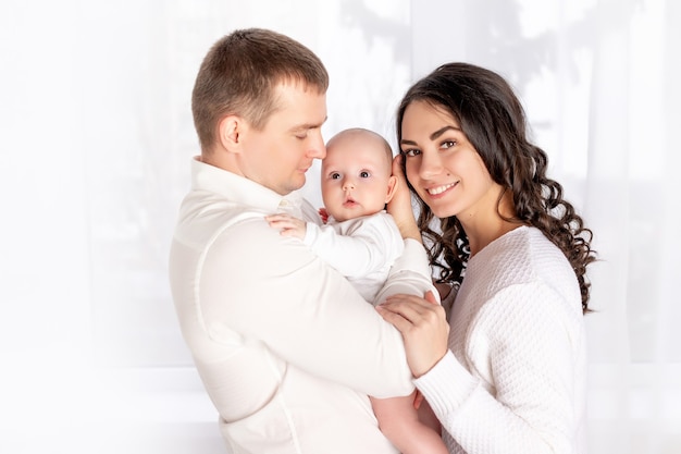 Happy young family with newborn baby at home by the window, happy loving family concept