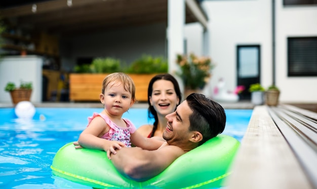 Счастливая молодая семья с маленькой дочерью в бассейне на открытом воздухе в саду заднем дворе.