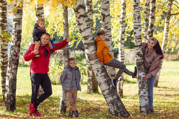 Felice giovane famiglia con tre bambini nel parco i figli si siedono sugli alberi in un boschetto di betulle amore e tenerezza