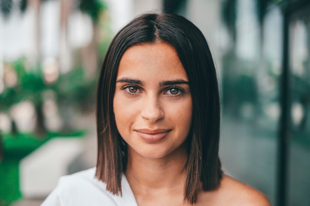 Happy young fashionable woman with short hair looking at camera outdoors. Beautiful satisfied lady with short hair smiling while facing camera. Portrait of confident female youth smiling