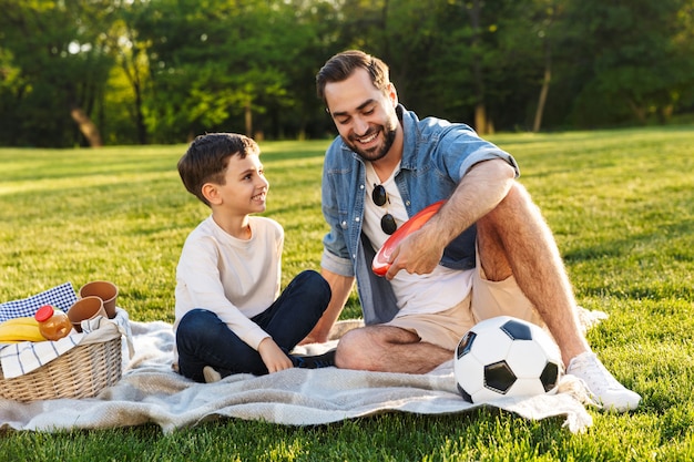 Счастливый молодой отец на пикнике со своим маленьким сыном в парке, разговаривает