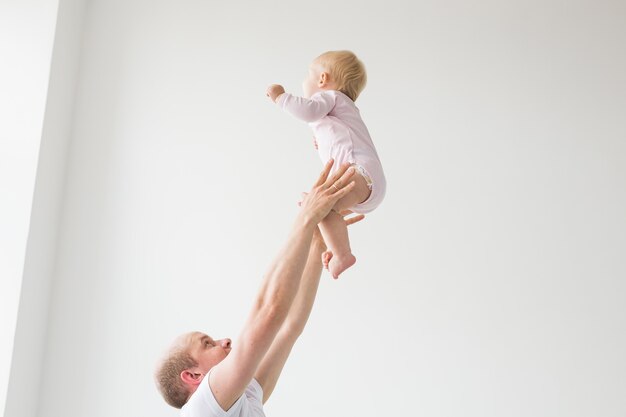 Happy young father lifting cute baby up high in air, spending and enjoying time together with