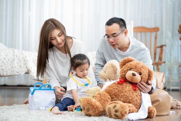 Happy young father and mother and a little daughter playing with Toy, sitting on the floor in living room, family, parenthood and people concept