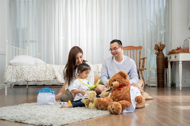 Happy young father and mother and a little daughter playing with Toy, sitting on the floor in living room, family, parenthood and people concept