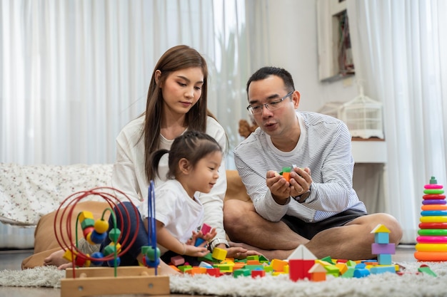 幸せな若い父と母と小さな娘が居間の床に座っているおもちゃの木製ブロックで遊んでいる家族の親子関係と発達おもちゃの人々の概念