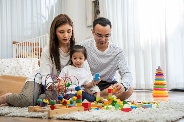 Happy young father and mother and a little daughter playing with Toy wooden blocks, sitting on the floor in living room, family, parenthood and people concept with Developmental toys