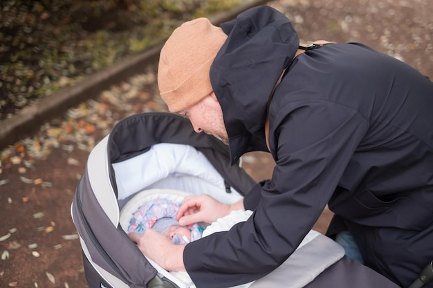 산책하는 동안 아기를 확인하는 유모차와 함께 행복한 젊은 아버지