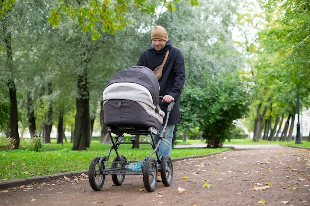 公園で自然の中を散歩中に乳母車で幸せな若い父親