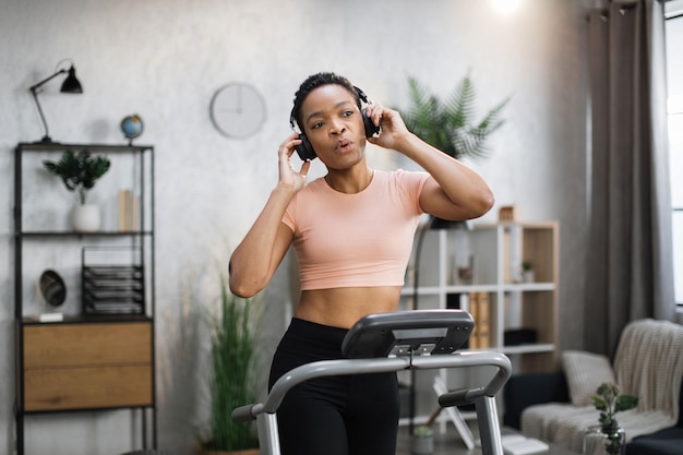 Happy young female athlete jogging on treadmill at home