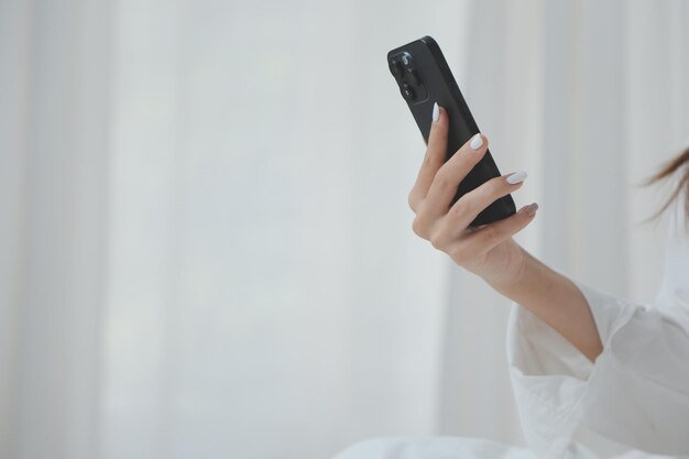 Happy young female in casual clothes smiling and looking at camera while using laptop on bed in bedroom at home