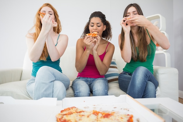 Giovani amici femminili felici che mangiano pizza a casa